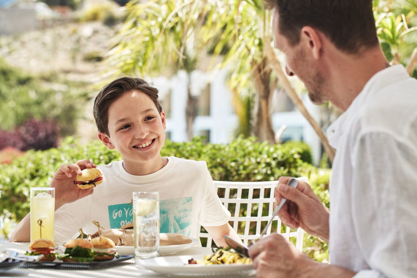 Boy enjoying his meal in the garden with his father at the Best all-inclusive hotels in Rhodes for families by H hotels Collection