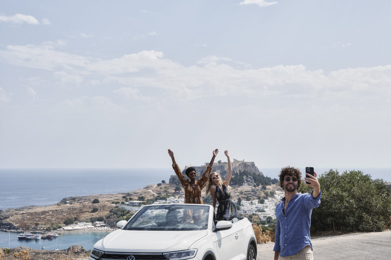 Group of friends posing with Lindos village in the background, one of the top places to discover on private tours in Rhodes with H Hotels Collection.
