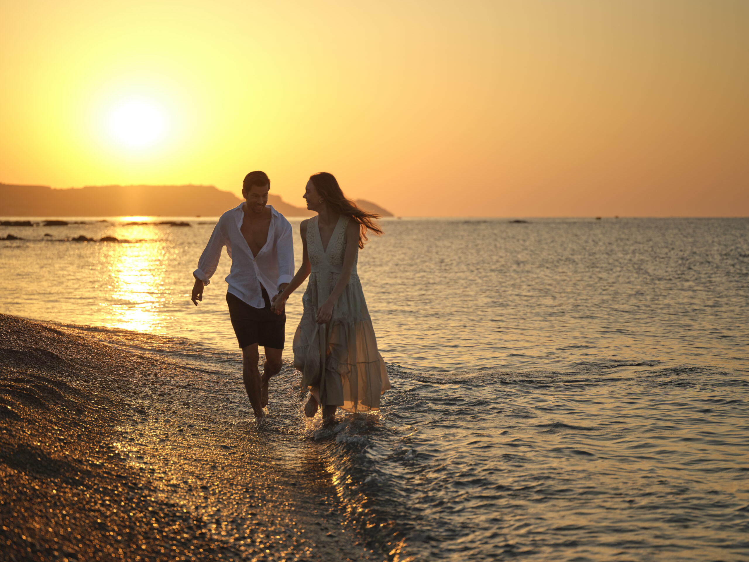 couple has a romantic walk at the beach on the sunset