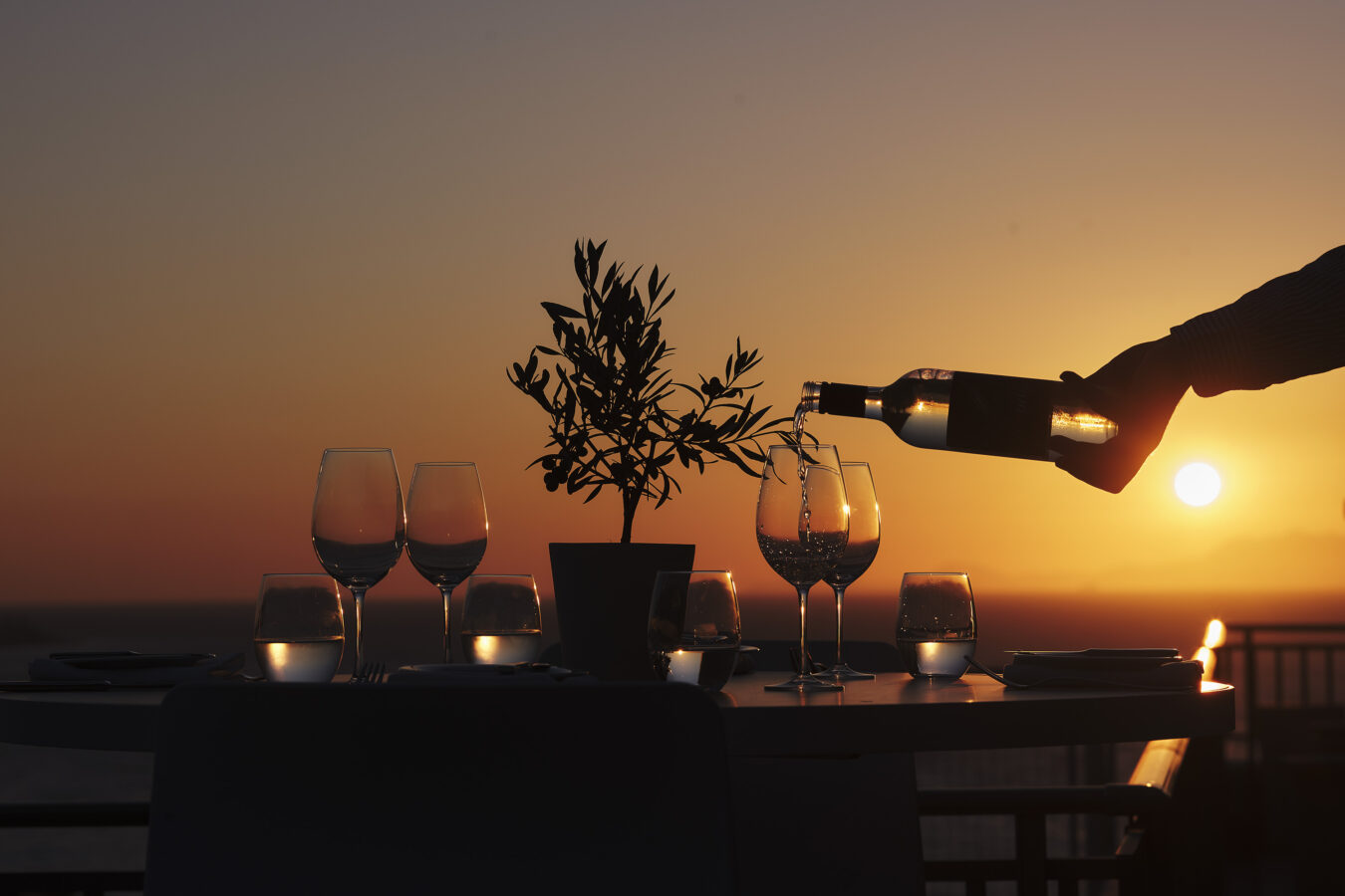 Sun setting over the sea and wine being served at one of the top restaurants in Ixia, Rhodes at Amus Hotel & Spa by H Hotels Collection.