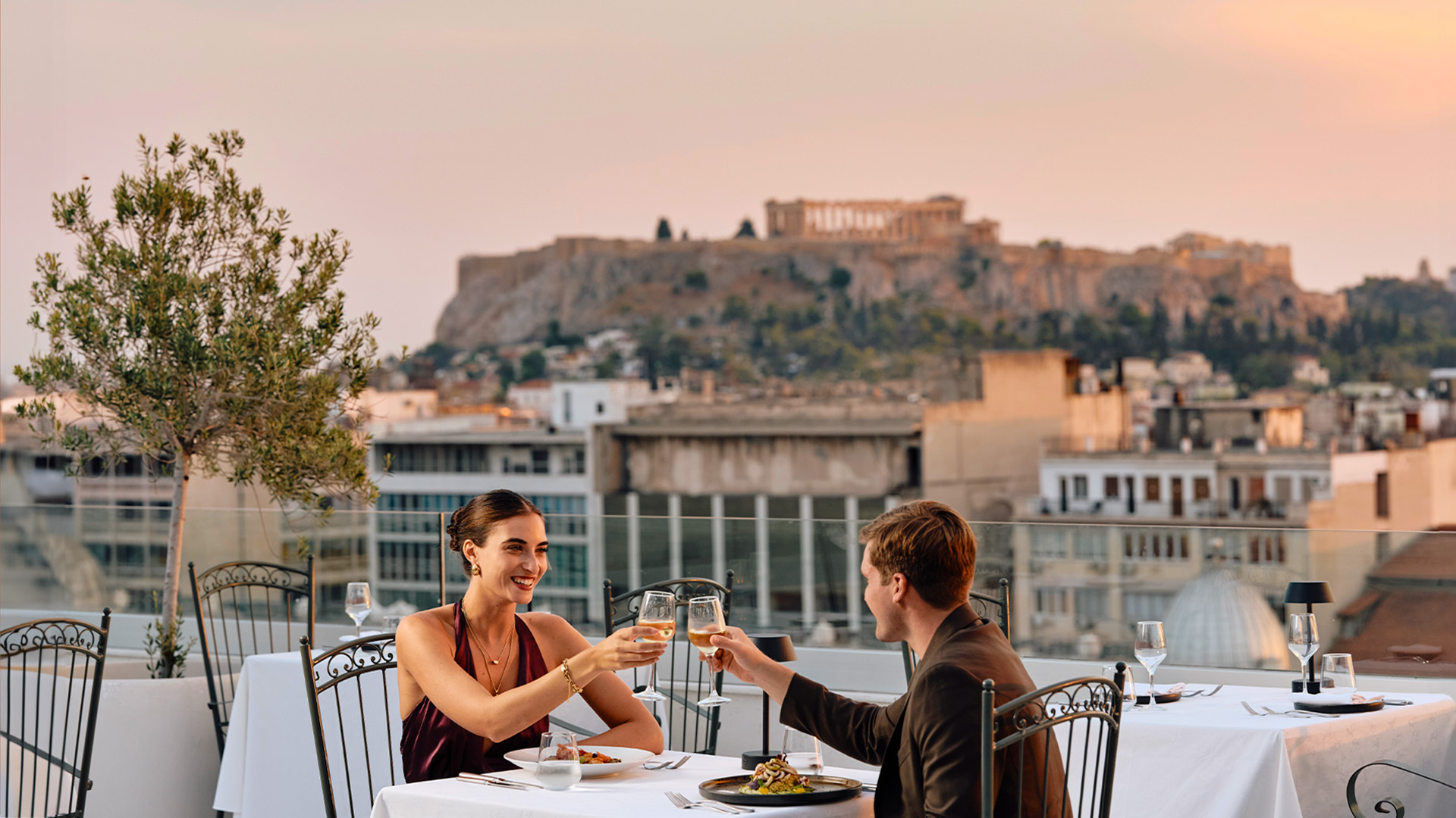 Toasting at dinner at the Olive Garden rooftop restaurant of Titania Hotel Athens with Acropolis views, one of the top things to do in Athens for couples.