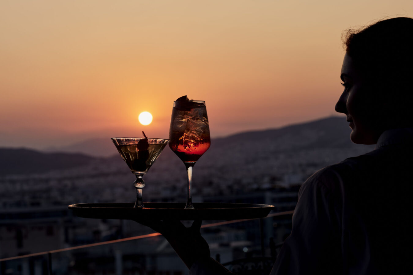 Cocktails pictured against orange sky during sunset in Athens, at the rooftop bar restaurant of Titania Hotel Athens, Olive Garden.