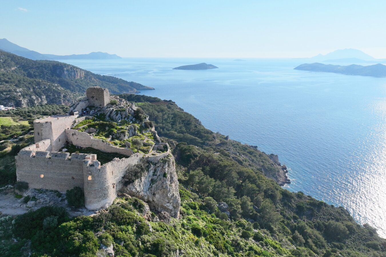 Aerial view of Kritinia Castle, one of the coastal Rhodes castles perched high on a green cliff overlooking the Aegean Sea.